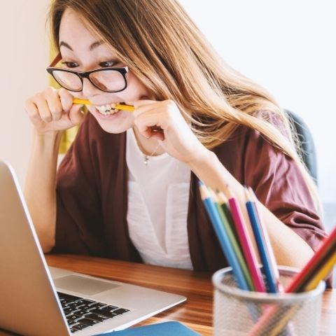 frustrated woman biting a pencil while looking at computer